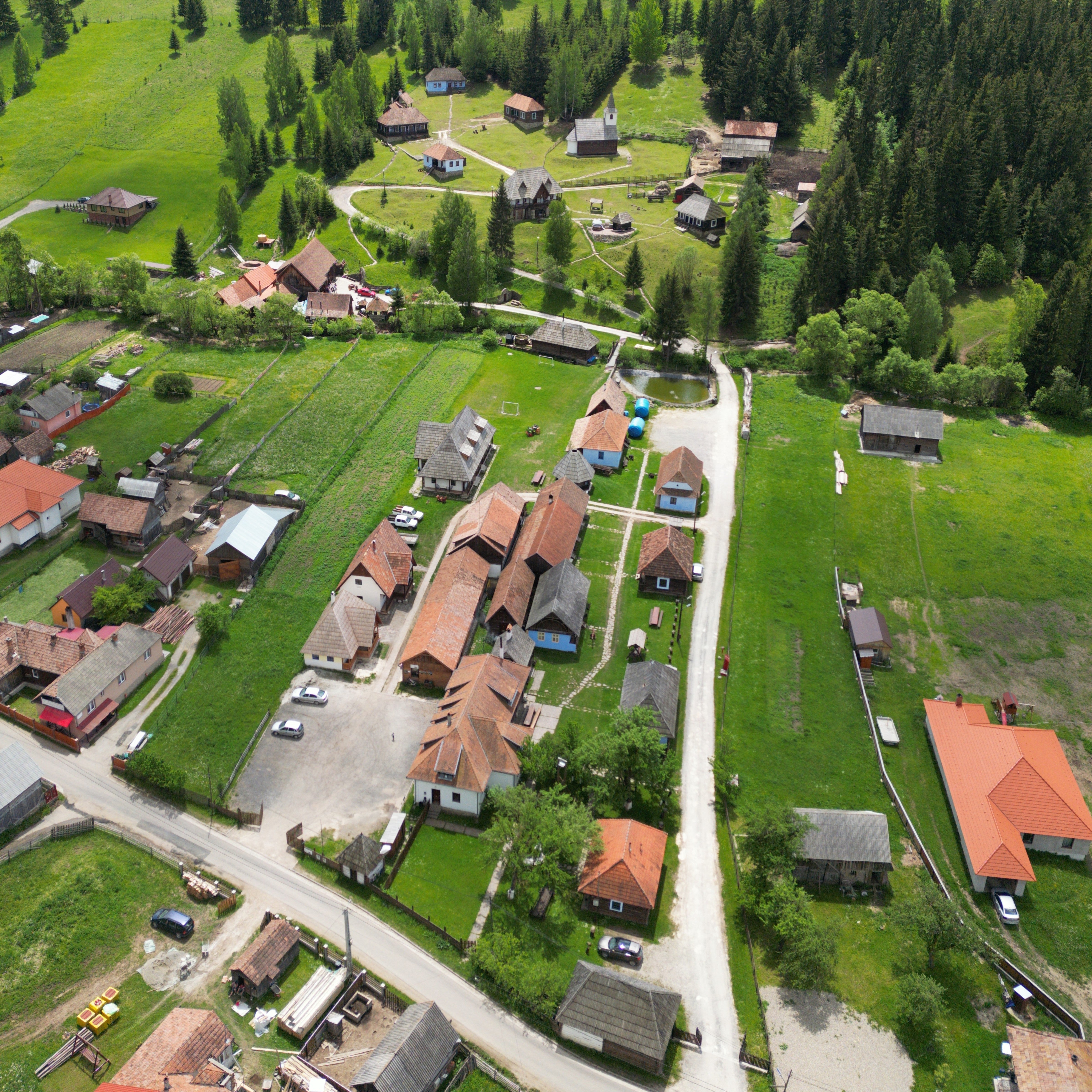 Aerial view of Gyimesi Skanzen with restored traditional houses surrounded by green hills and pine forests.