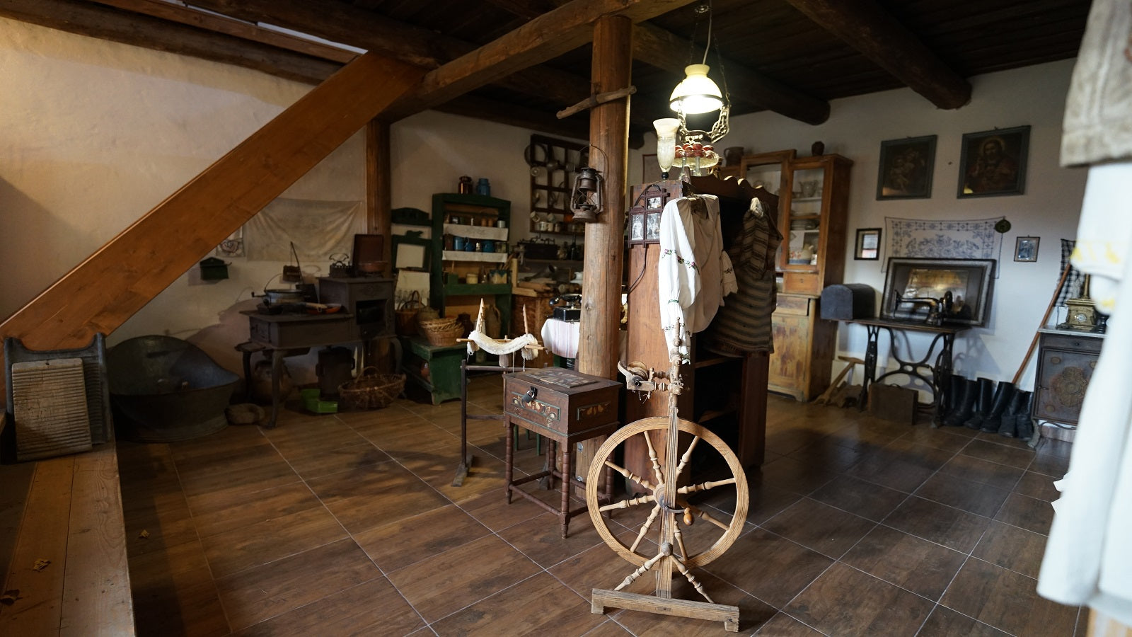 Museum room with an embroidered folk shirt and vest hanging by a wood post, a spinning wheel, and an old iron stove.