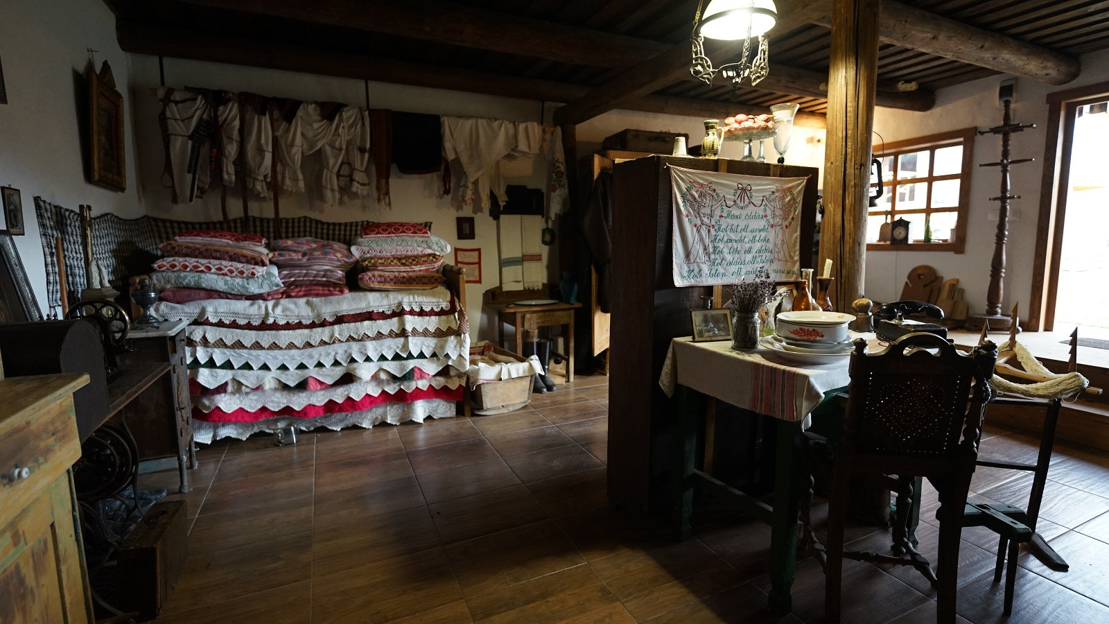 Museum bedroom display with a bed piled high with folk-embroidered pillows and cloths hanging on the wall above.
