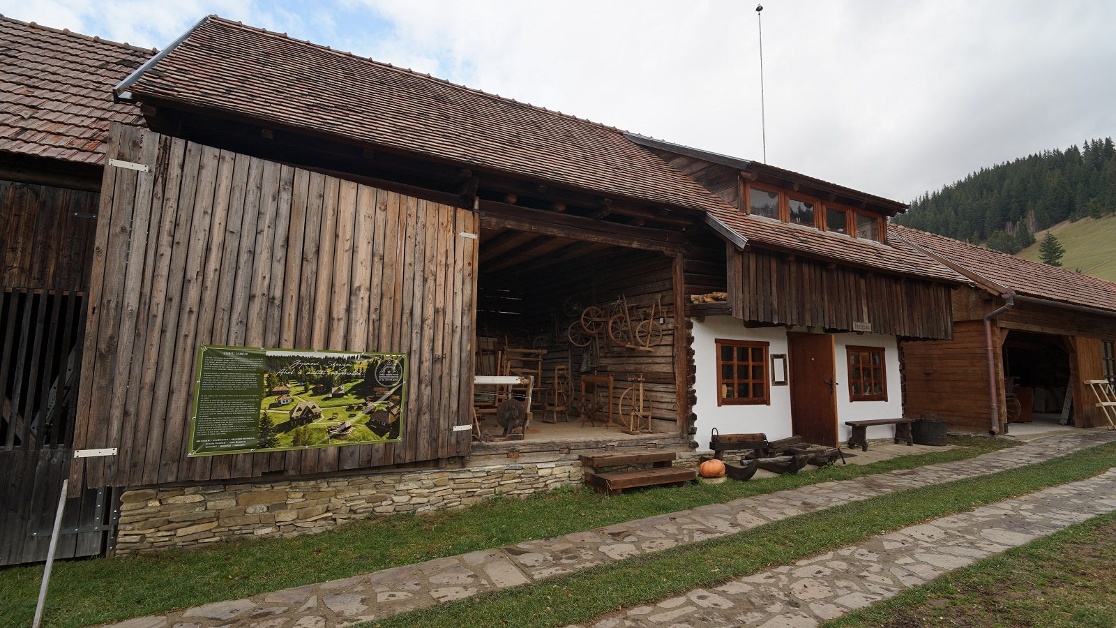 Exterior of the wood-shingle building with its barn doors open, revealing looms and spinning wheels inside.