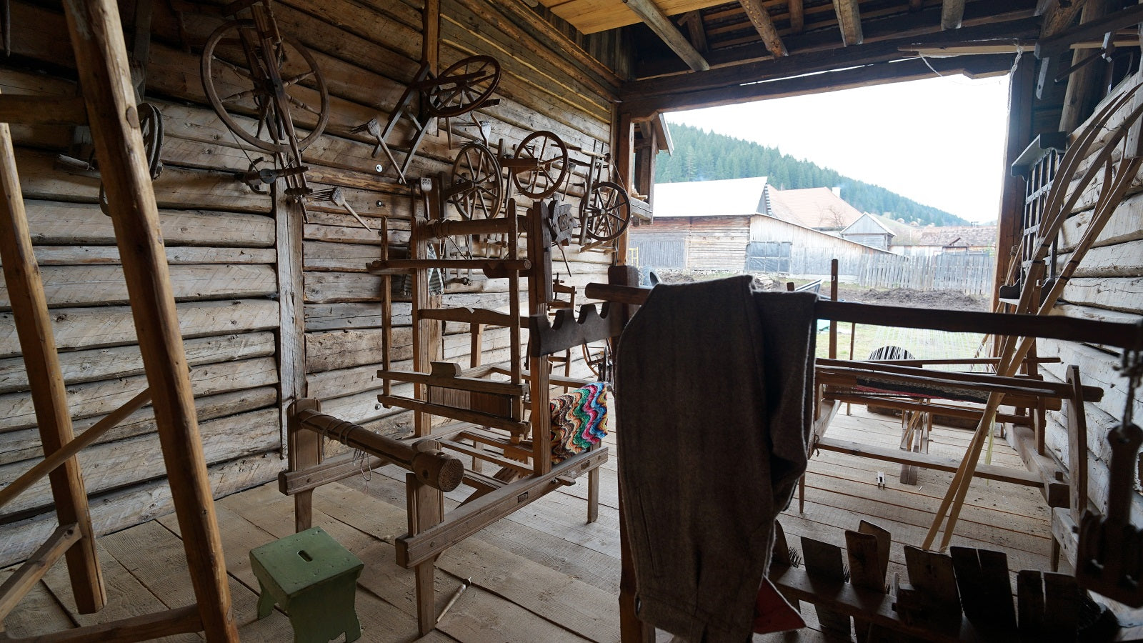 Workshop room with wooden looms and spinning wheels mounted on the log wall, opening onto a mountain view.