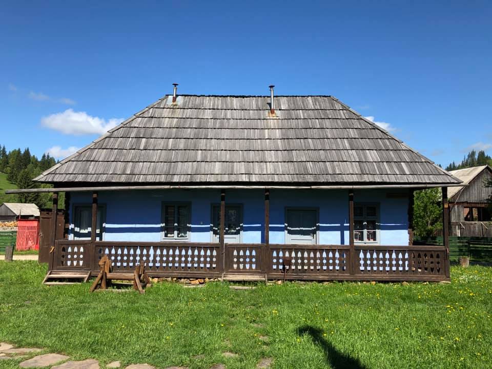 Front view of the Nagygyimesi house showing its full wraparound porch under a clear blue sky.