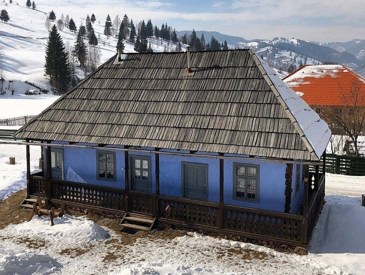Nagygyimesi house covered in snow, with mountains and an orange-roofed building in the background.