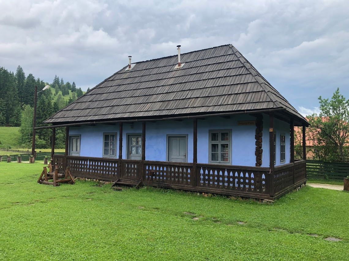 Nagygyimesi guesthouse, a blue house with a large dark wood shingle roof and pierced-lattice porch railing.