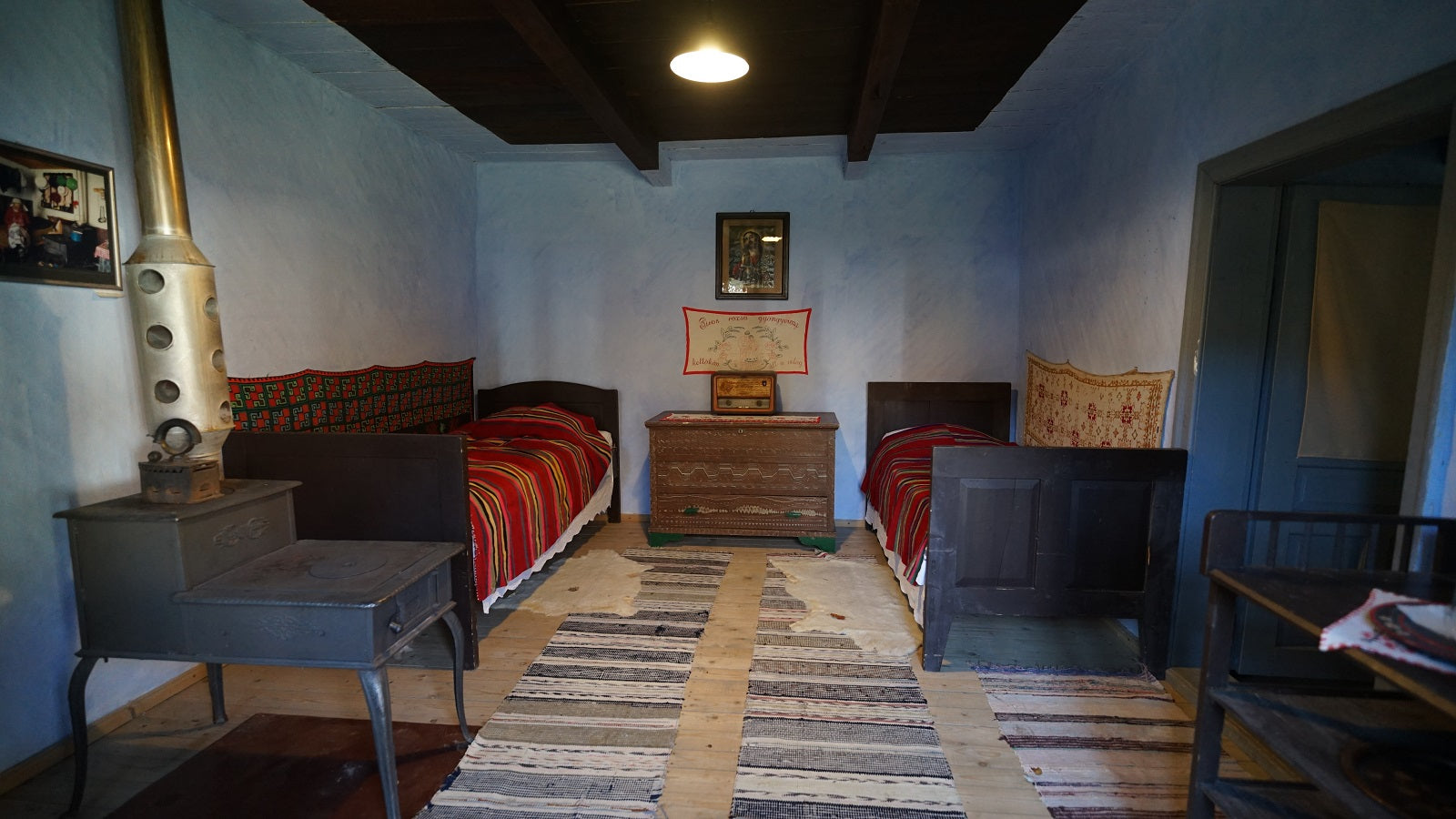 Bedroom with two dark wood beds in red striped throws, a cast-iron stove, and a carved wooden dresser.