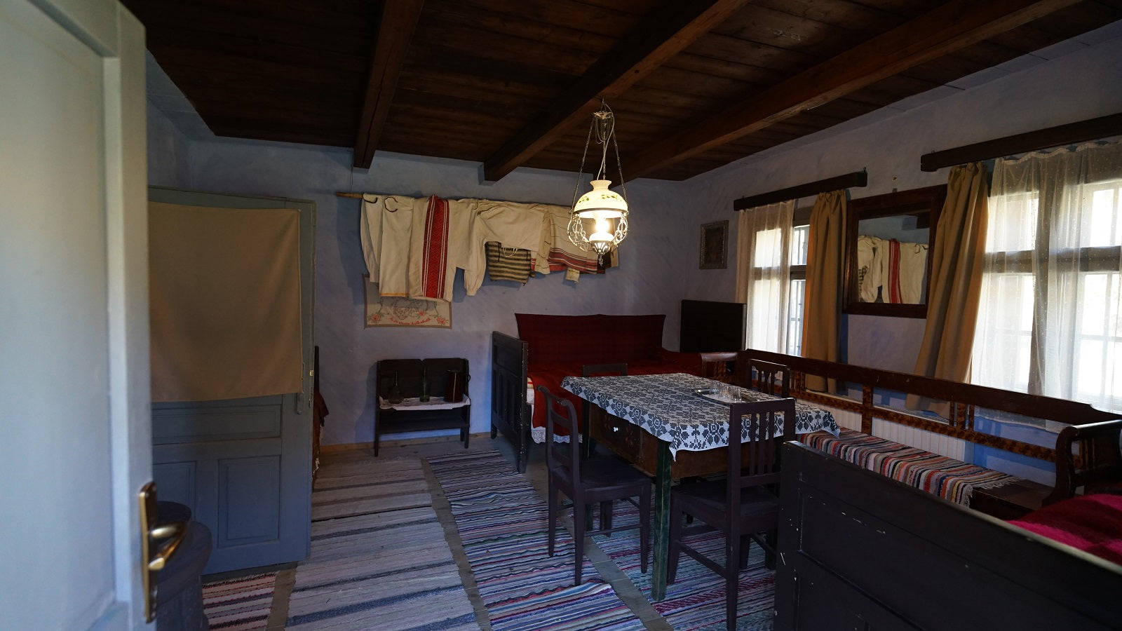 Room with embroidered traditional shirts hanging on display, a lace-clothed table, and a mirror.