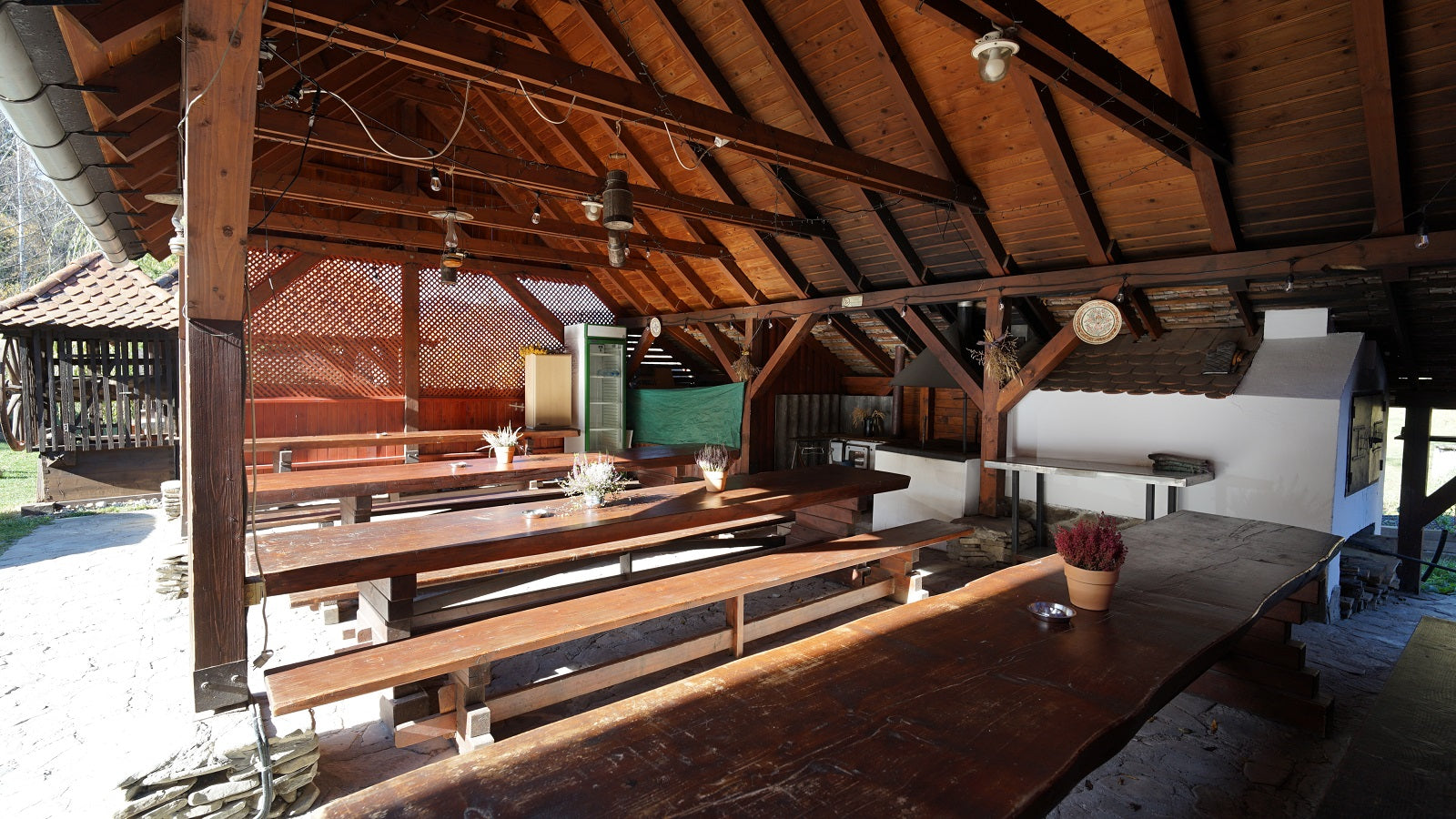 Covered outdoor terrace of the barn with long wooden tables and benches, and an outdoor hearth and kitchen counter.