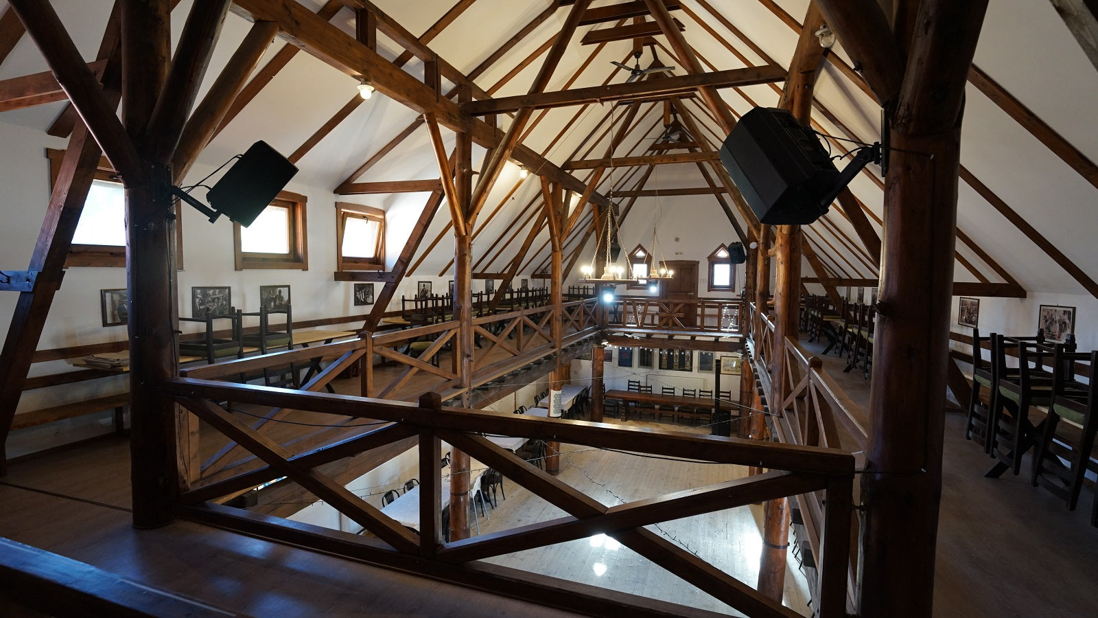 View across the barn's mezzanine level toward the opposite gallery, framed by wooden roof trusses and stained-glass windows.