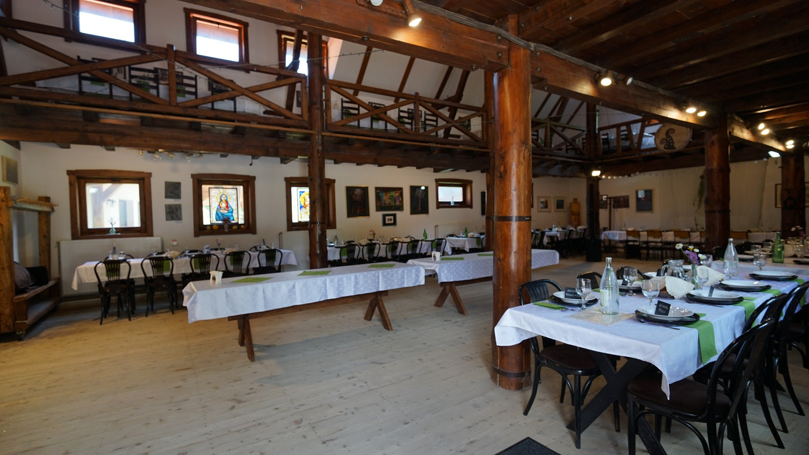 Daytime view of the barn set with tables in white linens and green accents beneath stained-glass windows and the mezzanine.