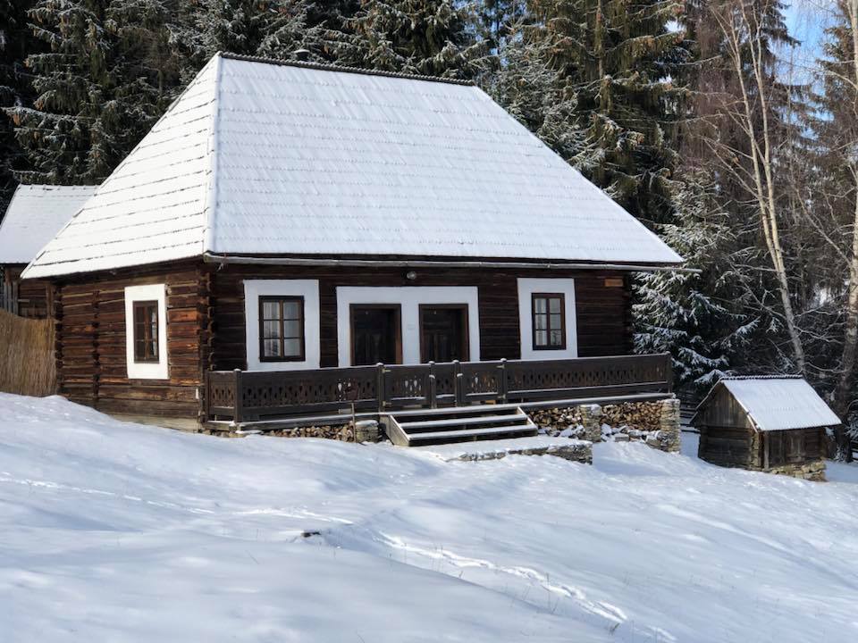 Snow-covered Tarhavasi house in winter, with a small stone-and-wood shed beside it.