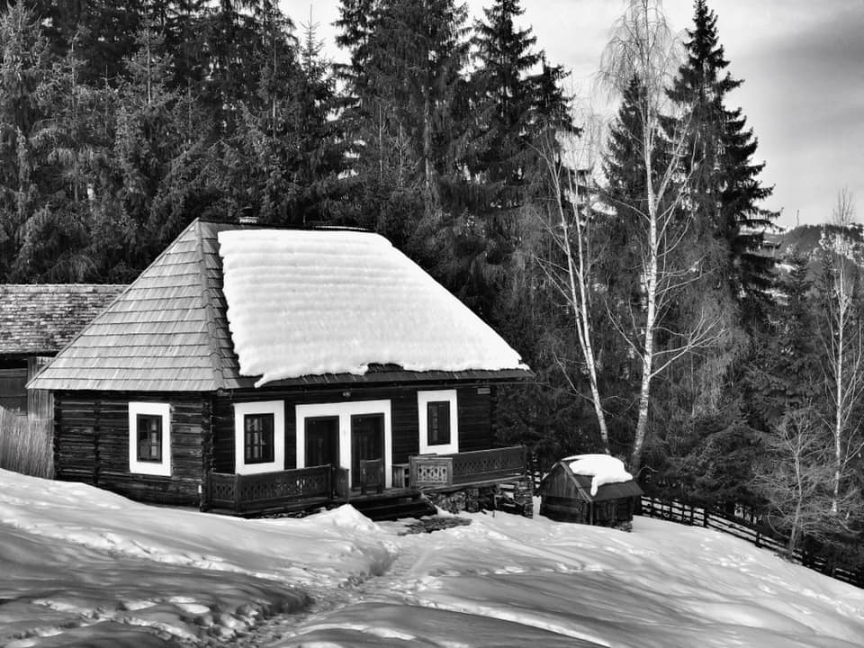 Black-and-white winter photo of the snow-covered Tarhavasi house, with footprints leading through the snow.