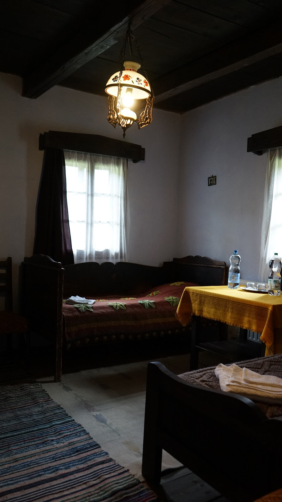 Dimly lit room with dark wood benches, a maroon leaf-pattern throw, and a yellow tablecloth on a small table.